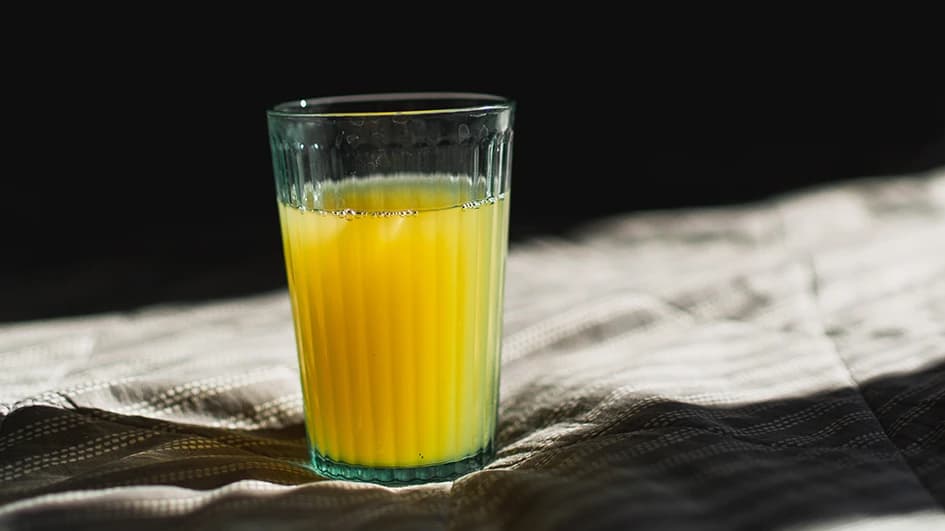 Verre de jus d'orange en gros plan, éclairé par une lumière rasante sur une nappe rayée devant un fond noir