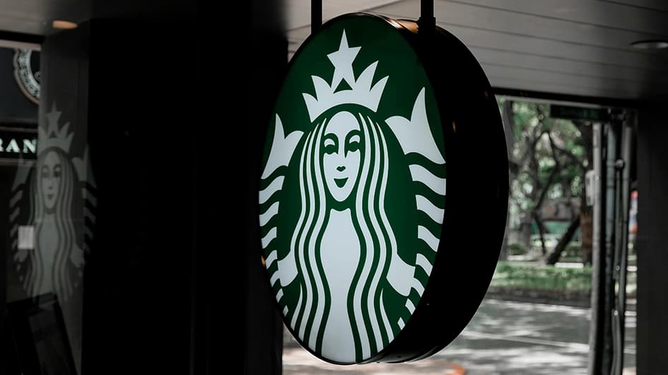 Enseigne ronde Starbucks à la sirène blanche sur fond vert, suspendue à l’entrée d’un café