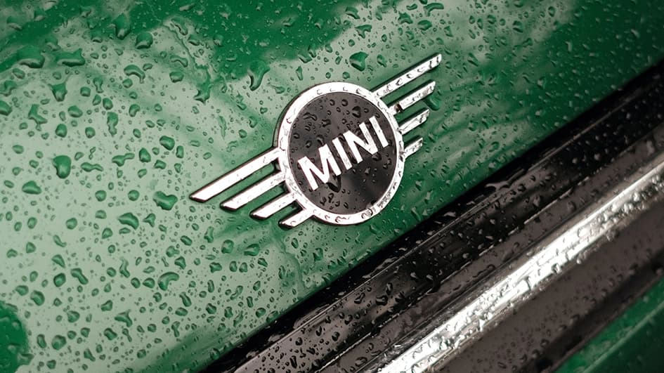 Logo MINI chromé sur le capot vert bouteille d’une Mini Cooper couvert de gouttes de pluie