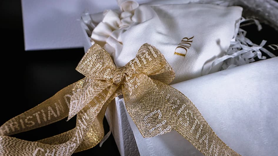 Coffret cadeau Dior noué d'un ruban doré pailleté « Christian Dior », pochette en tissu blanc brodée d'or