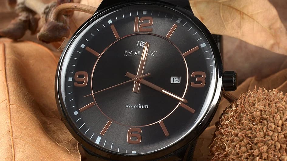 Montre au cadran noir et aux index cuivrés posée sur des feuilles mortes, le noir comme couleur du luxe