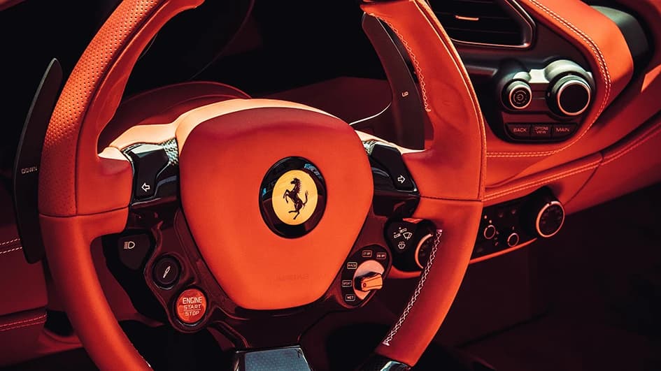 Volant d'une Ferrari en cuir rouge orangé, logo au cheval cabré sur fond jaune au centre