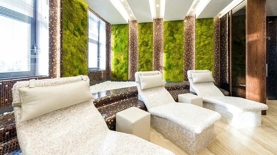 Salle de repos d'un spa avec trois transats en mosaïque nacrée, murs de mousse végétale et colonnes de mosaïque brune