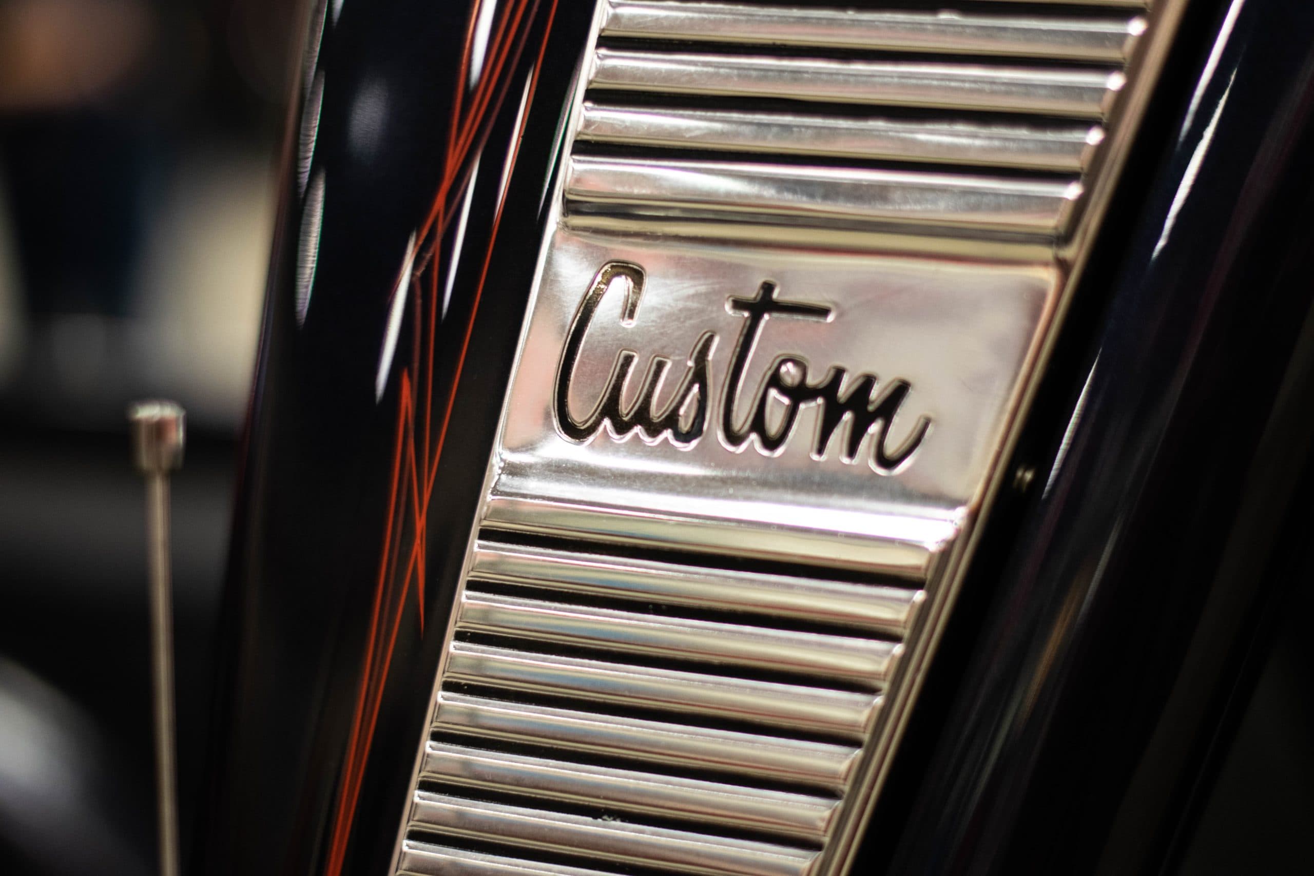 Emblème chromé « Custom » en lettres cursives sur le réservoir noir d'une moto, exemple de logotype script