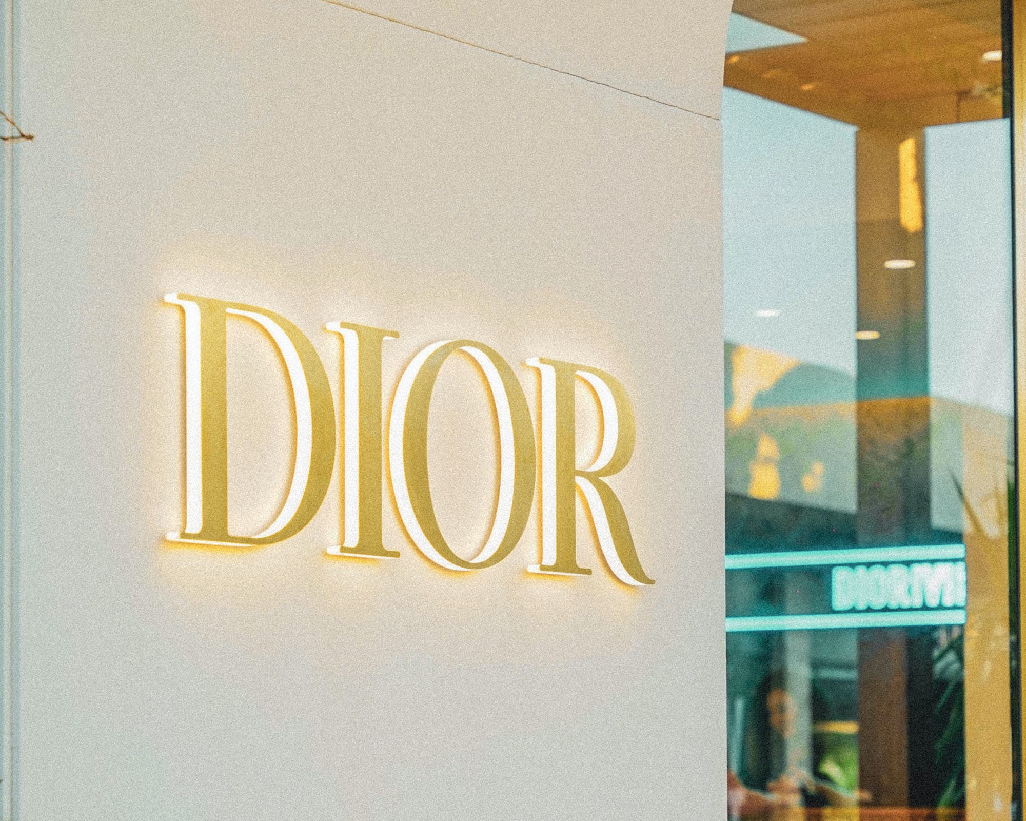 Enseigne Dior en capitales à empattements dorées et rétroéclairées sur la façade claire d'une boutique