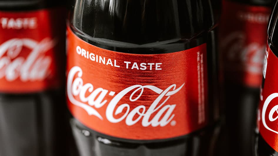 Étiquette rouge Coca-Cola « Original Taste » sur une bouteille en verre, logotype en écriture cursive blanche