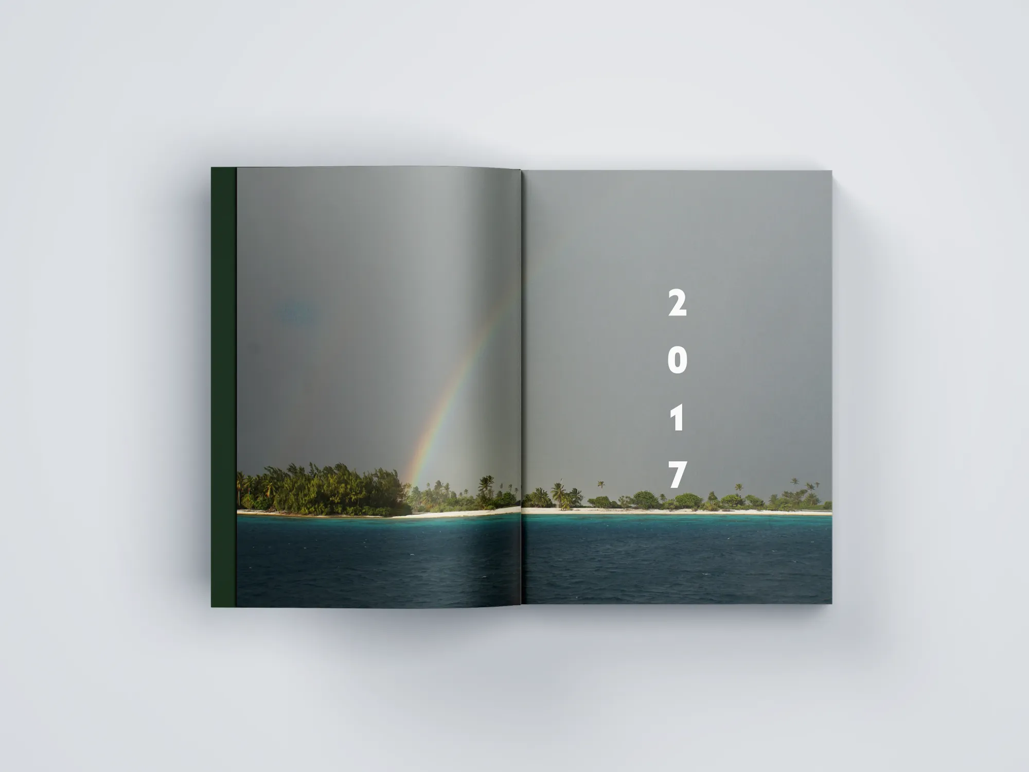 Ouverture de l'année 2017 du beau livre de voyage : atoll sous un arc-en-ciel en pleine double page, millésime composé à la verticale