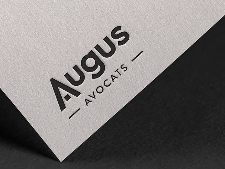Papier à lettres blanc texturé imprimé du logo noir Augus Avocats, posé en angle sur un fond sombre