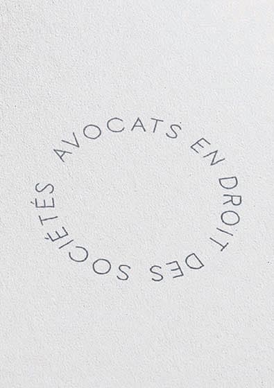 Mention « Avocats en droit des sociétés » imprimée en cercle sur papier blanc, déclinaison typographique d’Augus Avocats
