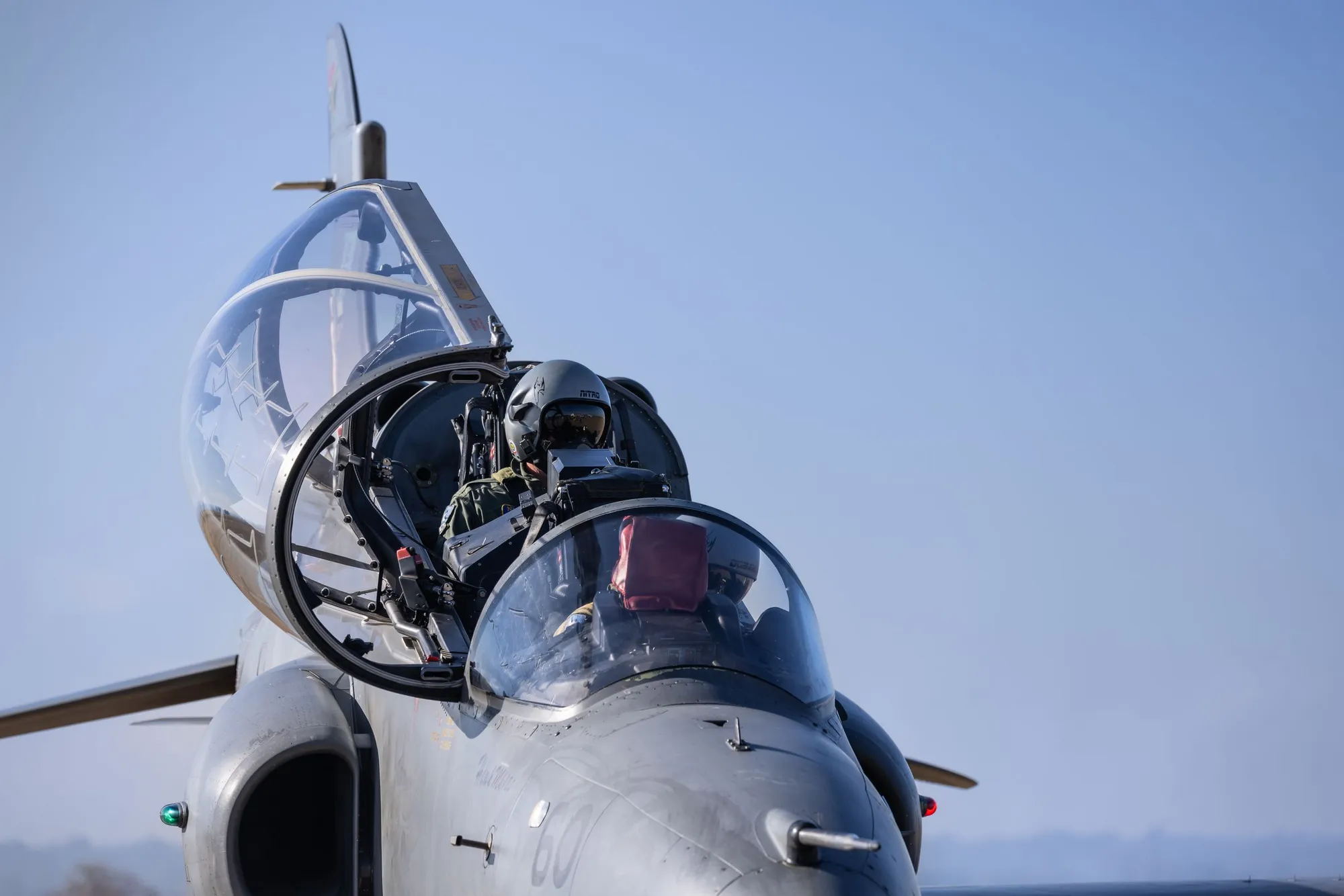 Pilote casqué installé dans le cockpit d'un avion de chasse, verrière ouverte sous un ciel bleu