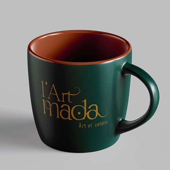 Mug vert sapin à l’intérieur terracotta, marqué du logo doré L’Art Mada et de sa baseline « Art et cetera »