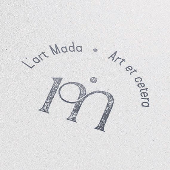 Tampon circulaire L’Art Mada à l’encre bleue sur papier blanc, monogramme lm entouré de « Art et cetera »