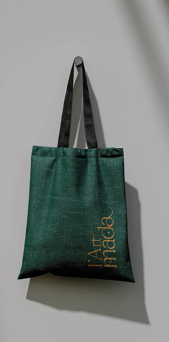 Tote bag en toile vert sapin suspendu à une patère, logo L’Art Mada imprimé en doré à la verticale