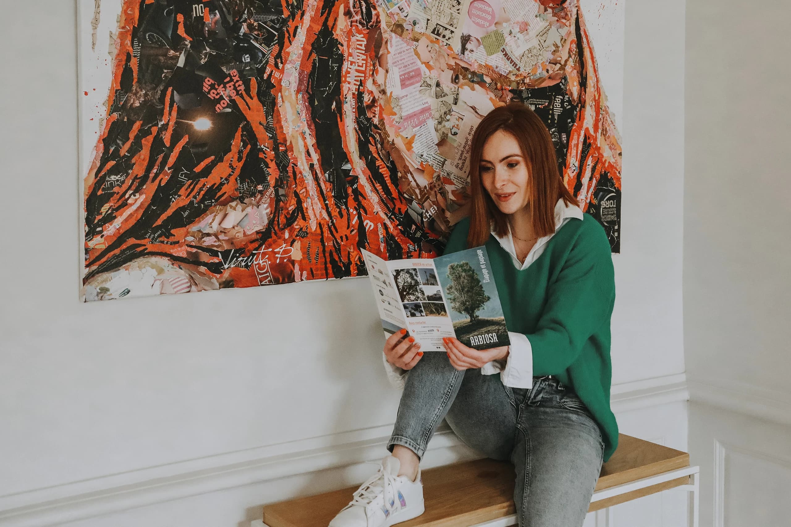 Fanny Métivier, graphiste à Nantes, feuillette un dépliant Arbiosa, élagage et paysage, assise sous un grand collage